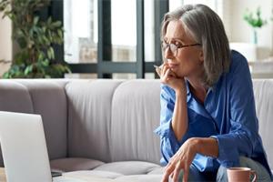 A woman sitting on a couch looking at a computer.
