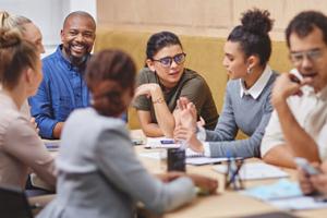 Diverse group of adults sitting at long table having discussions