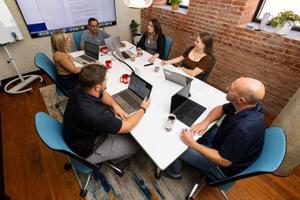 People sitting at conference table talking and working on laptops.