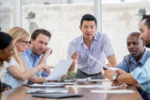 Group of professionals at conference table discussing and reviewing papers together.