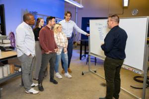 Instructor standing at whiteboard talking with several adult class participants.