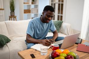 A man taking notes at a computer with fruit in the foreground