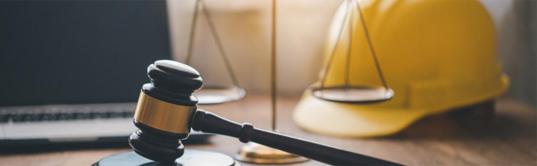 A gavel on a table with legal scales and a hard hat behind it.