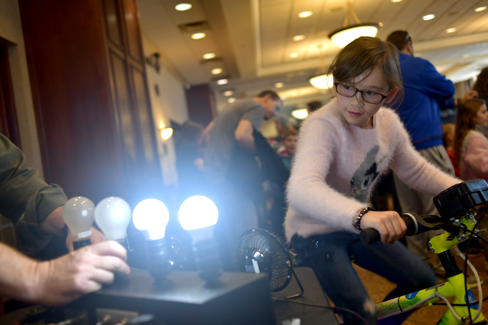 Alyssa Chiang, 8, turns muscle power into electricity. The bulbs on the right are brighter because they are more energy efficient. It takes a lot more effort to make the incandescent bulbs glow. Photo by Michael Hicks.